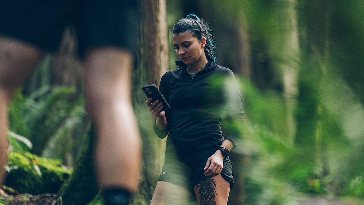 Trainingpeaks Coach Payments Image Of A Young Female Runner In The Woods Stopping On The Trail To Look At Her Phone To Check On Trainingpeaks Coach Payments