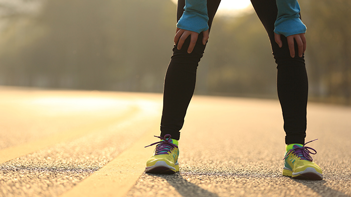 Tired Endurance Athlete In Need Of Recovery Runner Holding Knees And Taking A Break On Road