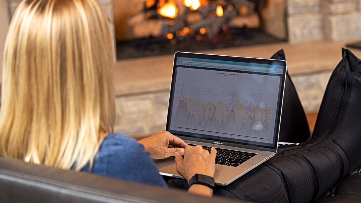Athletic Woman Analyzes Her Trainingpeaks Data Using The Latest Sports Tech Trainingpeaks Ambassador Uses Sports Tech On Her Laptop In The Living Room In Front Of The Fireplace