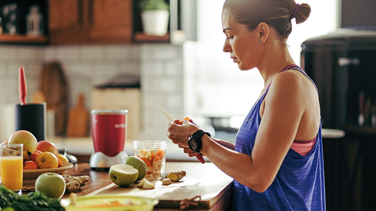 A Complete Guide To Marathon Nutrition Image Of An Athletic Woman Slicing Fruit While Preparing Smoothie In The Kitchen For Honing In On Her Marathon Nutrition