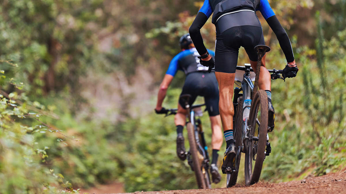 Here’s A Detailed Look At The Muscles Used In Cycling And How To Train Them Two Fit Cyclists Ride Down A Dirt Path Training Their Cycling Muscles